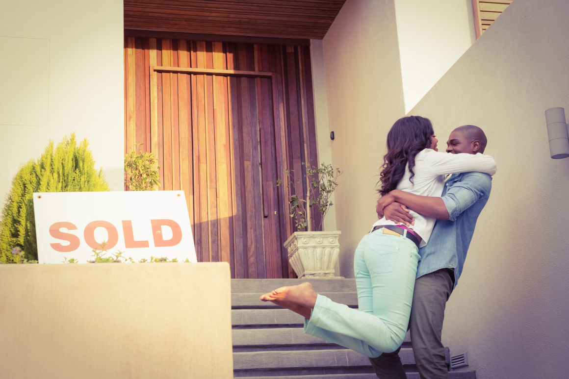 happy couple huging out side a home with a sold sign